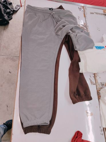 Two pairs of sweatpants, one gray and one brown, laid out on a white surface.