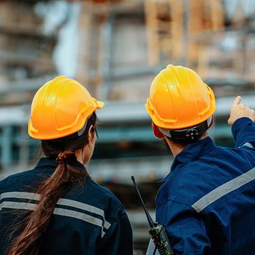 Dos trabajadores con cascos amarillos señalando una construcción.
