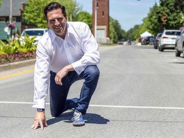 A man crouches on a street, smiling at the camera on a sunny day.