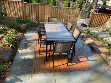 Outdoor patio with a dining table and six chairs on a wooden deck.