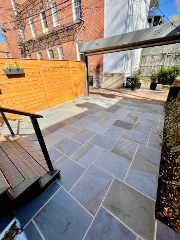 Clean, modern outdoor patio with stone tiles and wooden fence.