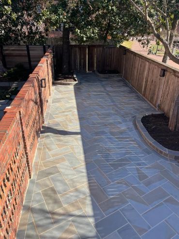 A clean, tiled patio with brick and wooden fencing and built-in tree planters.