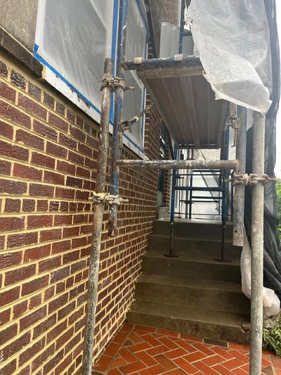 Scaffolding set up around brick building with covered windows and stairs.