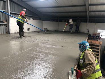 Workers smoothing freshly poured concrete inside a building under construction.