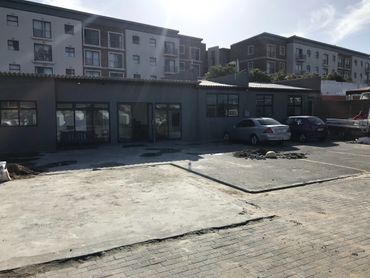 Parking lot in front of a gray building with cars and a bench.