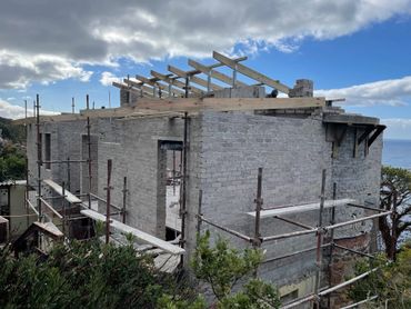 A brick house under construction with wooden roof beams and scaffolding.