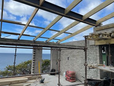 Construction site overlooking a body of water with wooden beams and masonry walls.