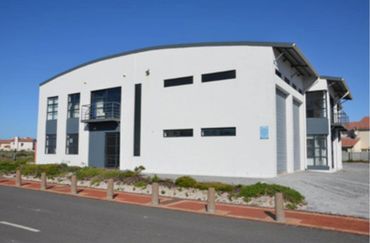 Modern white commercial building with curved roof and large windows under clear blue sky.