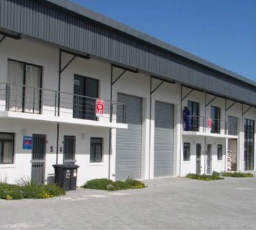 A modern industrial building with multiple units and roller doors under clear blue sky.
