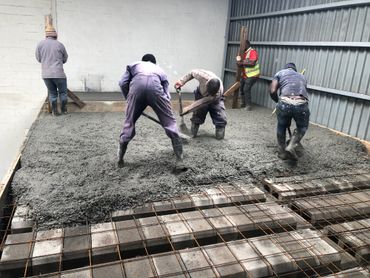 Workers leveling freshly poured concrete inside a building under construction.