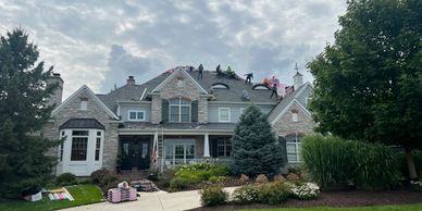 Workers installing a new roof on a large suburban house under a cloudy sky.