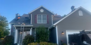 Two-story house with ladders and roofing work in progress.