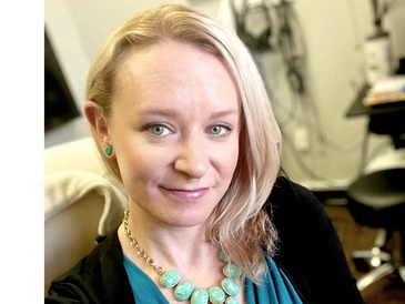 Smiling woman with blonde hair wearing a teal top and statement necklace. audiology care, hearing disorders, hearing aid repair service