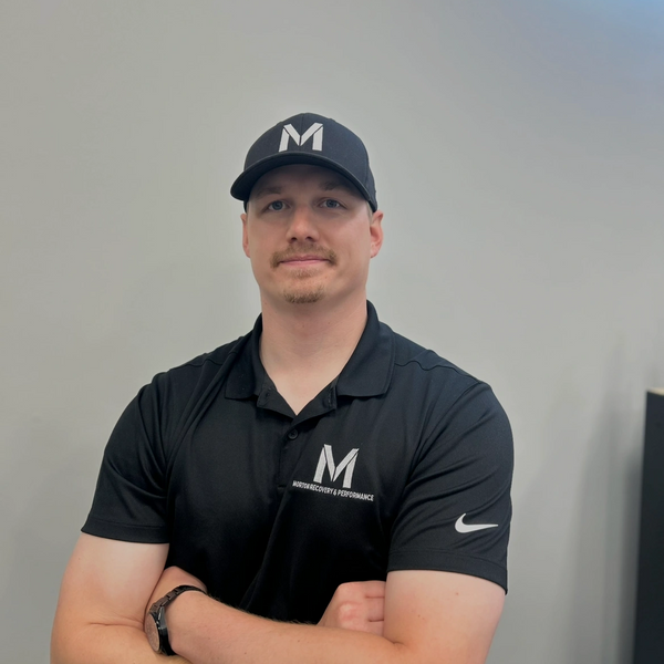 Man in black cap and polo shirt with logo, arms crossed.