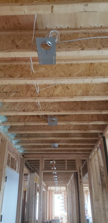 Framed hallway ceiling with electrical wiring and recessed light mounts in a building under construction.