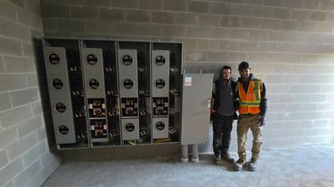 Two workers stand next to electrical panels in a construction site.
