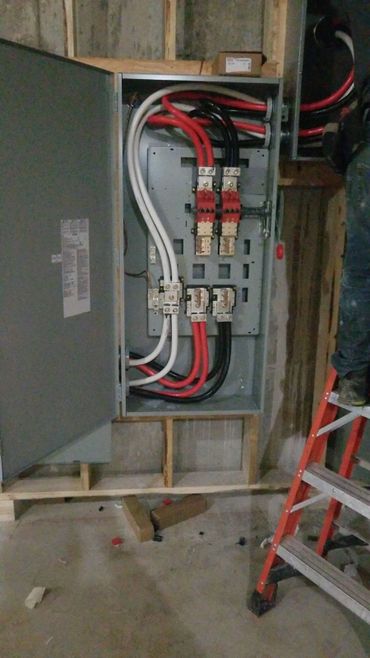 Open electrical panel with organized red, black, and white cables inside a construction site.