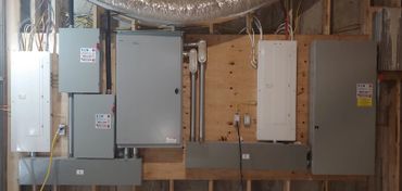 A series of electrical panels and circuit boxes mounted on a wooden wall.