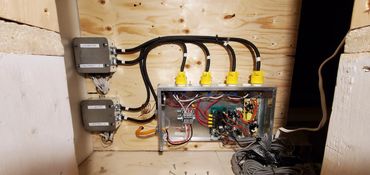 Electrical heater control boxes and wiring mounted on a wooden panel.