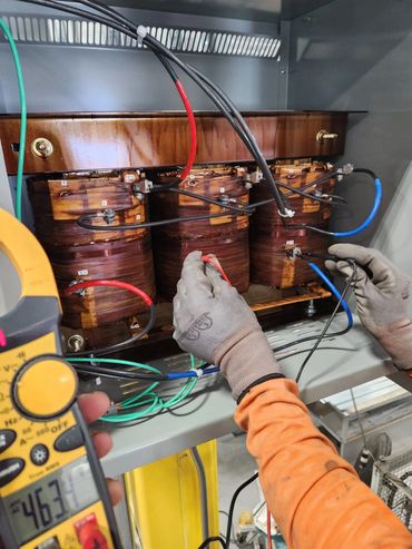 Technician testing electrical transformer with multimeter in industrial setting.