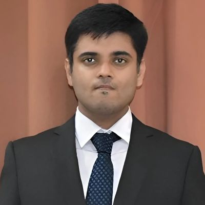 Professional man in a black suit and blue tie against a neutral background.