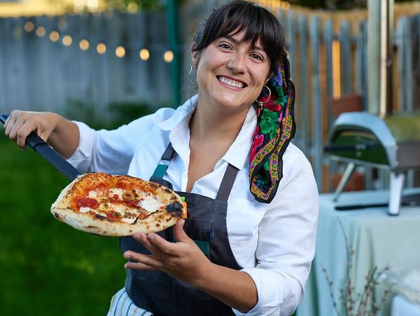 Smiling woman holding a freshly baked pizza outdoors.