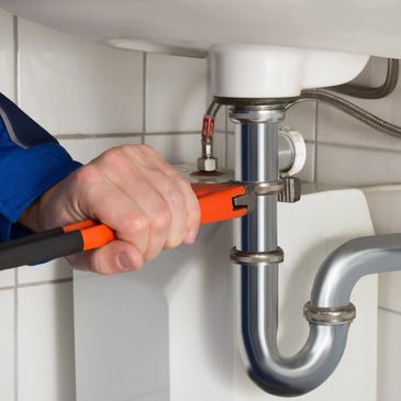 A plumber using a wrench to fix a sink pipe.
