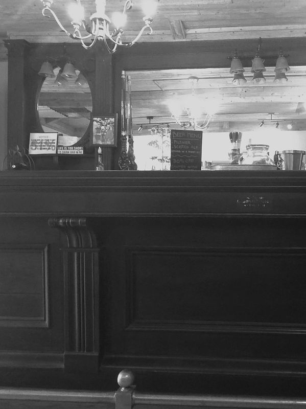 Black and white photo of a vintage bar interior with chandeliers and mirror.