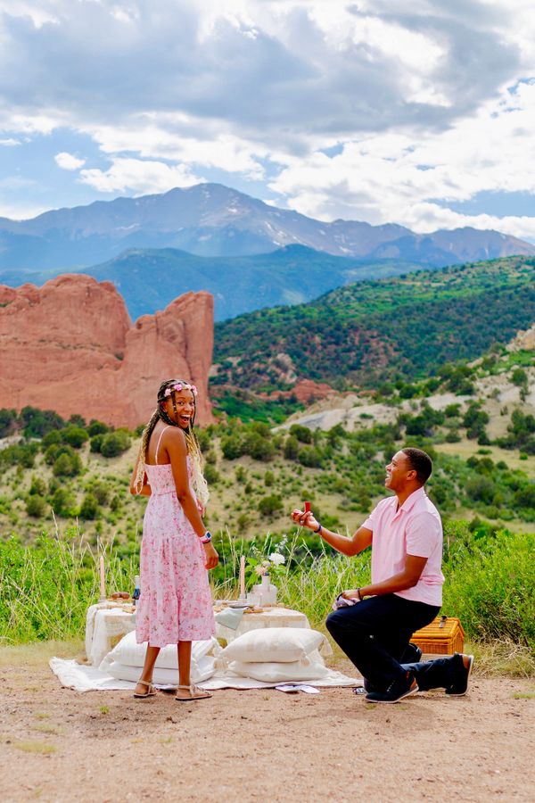 Man proposing to woman during a scenic outdoor picnic in the mountains.