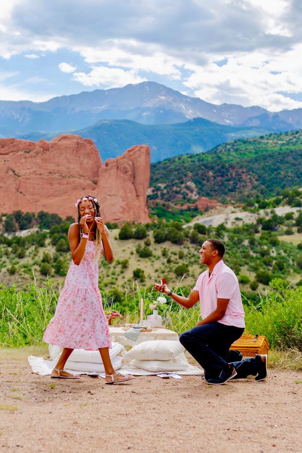 A man proposes to a woman during a picnic in a scenic mountainous area.