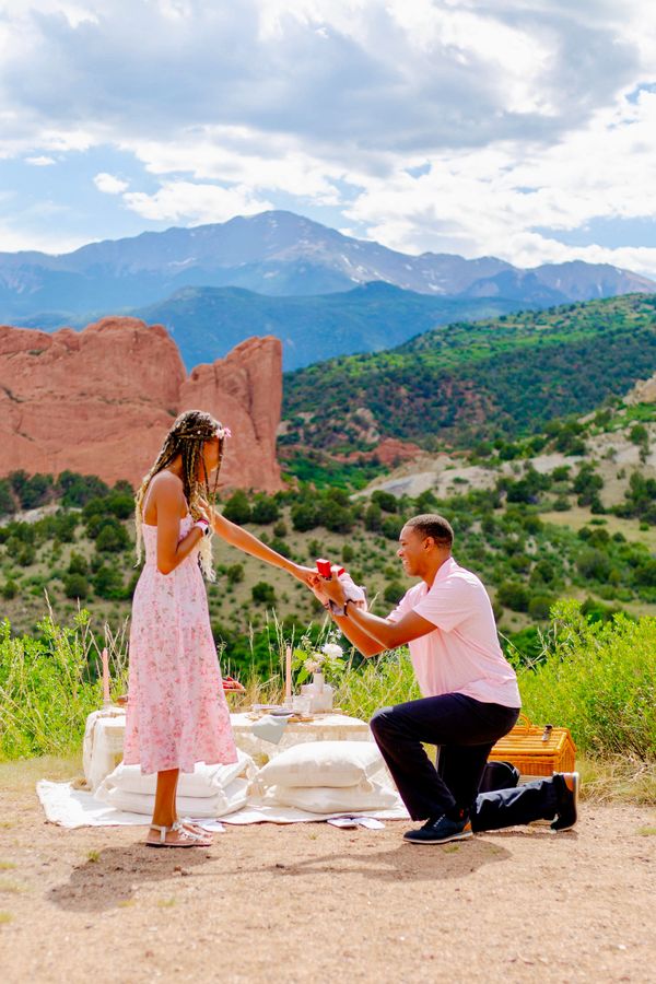 Man proposing to woman during a picnic in a scenic mountain area.