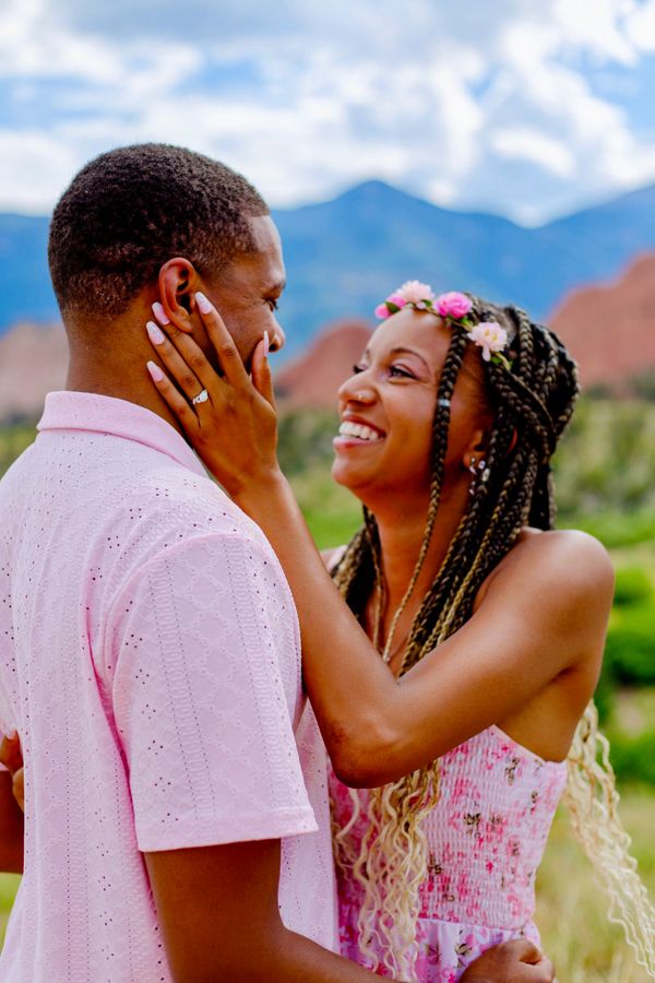 Couple joyfully embracing outdoors, woman showing engagement ring.