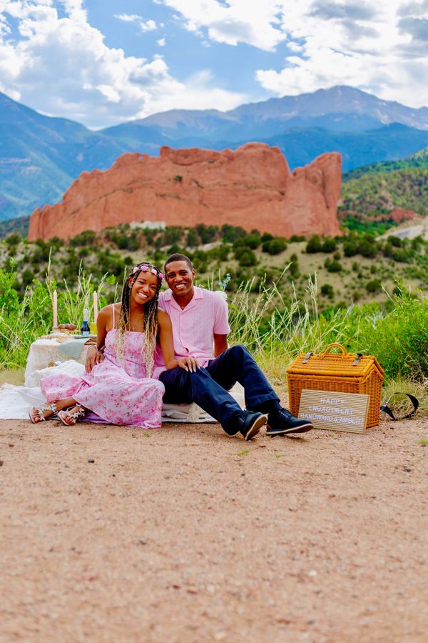 A happy couple celebrating their engagement outdoors with scenic mountain views.