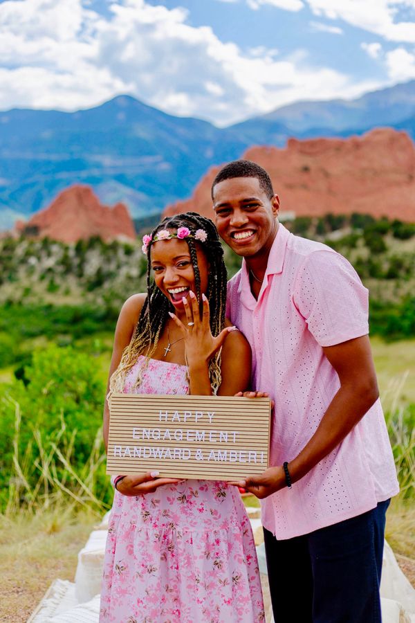 Happy couple celebrating engagement with a sign outdoors.