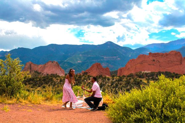 Man proposes to woman outdoors with mountains and red rock formations.