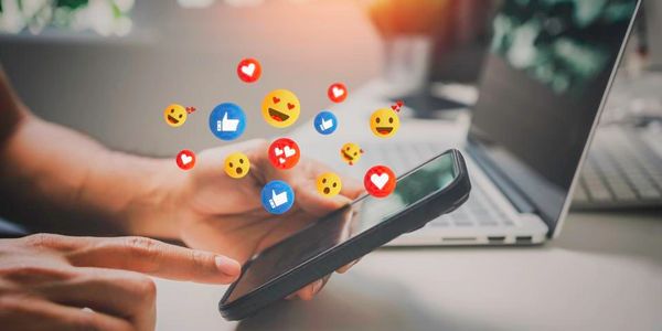 Person using smartphone with social media reaction icons floating around.