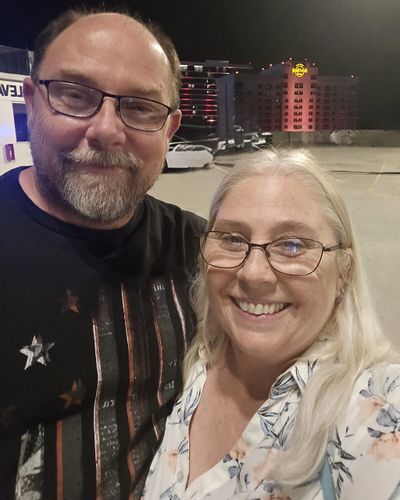 A couple smiling and taking a selfie at night in an outdoor parking area.
