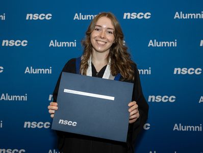Samantha McNeil holding her Graduate Diploma in Digital Marketing in front of an NSCC backdrop.