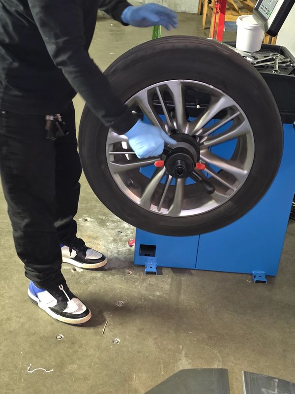 Person wearing blue gloves working on a car tire in a workshop.