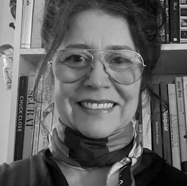 Smiling woman wearing glasses and a scarf in front of bookshelf.