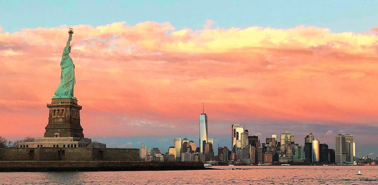 Statue of Liberty with New York skyline at sunset over the water. Photo by Marta Skrzynska