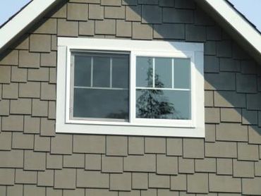 A white-framed window on a building with gray shingle siding.