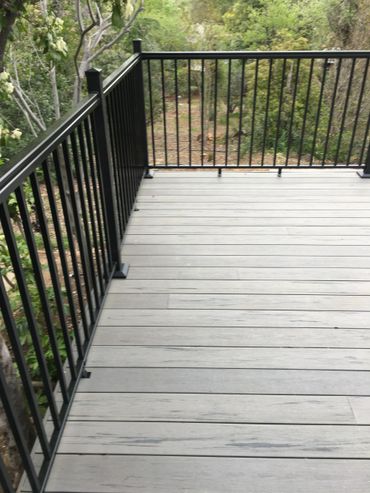 Empty outdoor deck with black metal railing overlooking greenery.