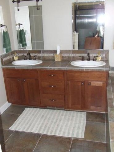 Double sink wooden vanity with brown tile countertop in a bathroom.