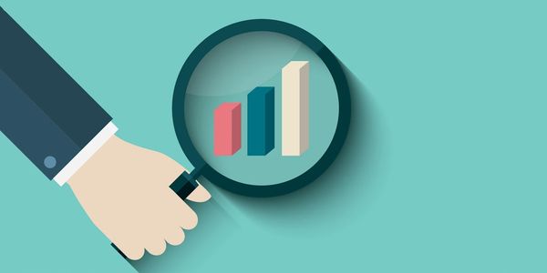 Hand holding magnifying glass over rising bar chart, symbolizing growth analysis.