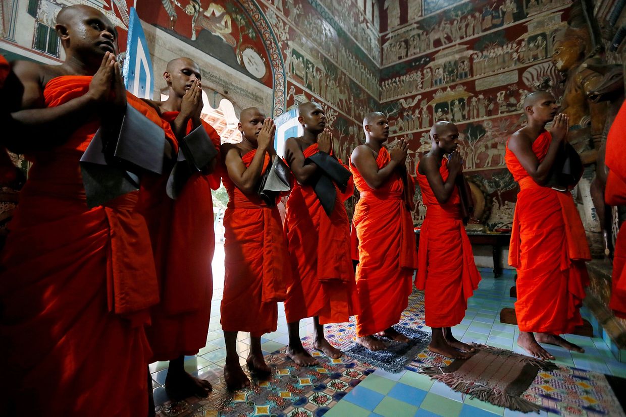 A group of Buddhist monks from Sri Lanka standing in a temple with hands together in prayer gesture.