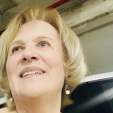 Smiling woman with blonde hair wearing a blue patterned top and gold necklace.