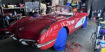Classic red convertible car in a garage with blue tire covers.