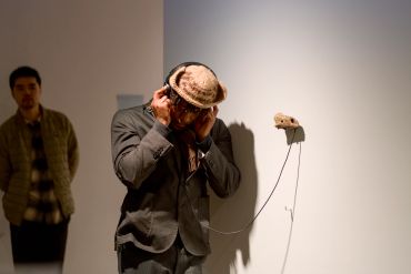 A man listens to headphones connected to a rock on a wall in an art gallery.