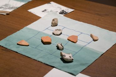 Stones placed on a hand-drawn grid on cloth, resembling a game setup.